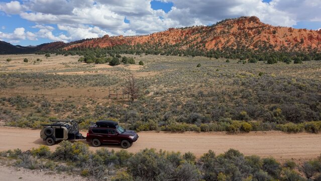 Aerial view of an SUV pulling a teardrop camper trailer on a dirt road through the red rock landscape of Costa Canyon near Bryce Canyon, Panguitch, Utah, United States.