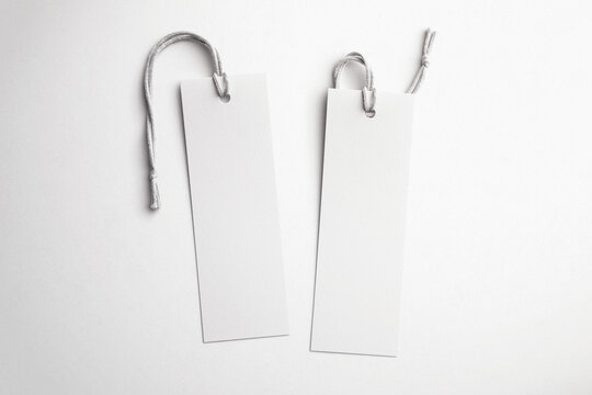 Two blank white paper bookmarks with string on a softly lit white background, top view mockup