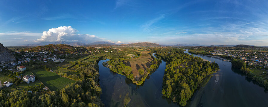 Aerial view of the confluence of the Drin and Buna rivers near Shkoder, featuring lush green riverbanks, surrounding hills, and a clear blue sky in Shkoder, Shkoder County, Albania.