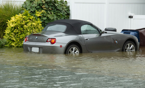Ventnor, New Jersey, USA, September 26, 2026, A silver BMW Z4 convertible sits partially submerged in brown floodwater in a residential driveway after heavy rain, illustrating storm damage, property f