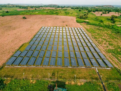 Aerial view of a large solar farm with rows of photovoltaic panels installed on a grassy field in a rural landscape in Ogun State, Nigeria.