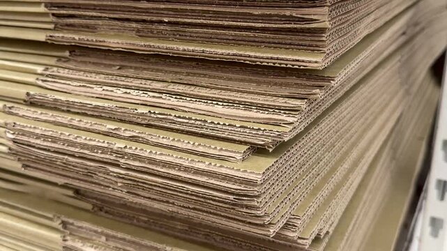 Stacked flat corrugated fiberboard sheets in a factory workshop. Industrial manufacturing background, eco friendly logistics packaging materials, textured brown paper.