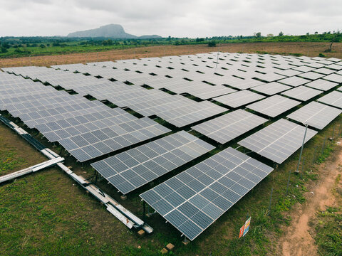 Aerial view of a large solar farm with rows of photovoltaic panels set in a rural landscape with a distant hill in Ogun State, Nigeria.