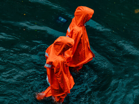 Aerial View of Two People in Orange Raincoats Wading Through Teal Floodwater, Monsoon Season