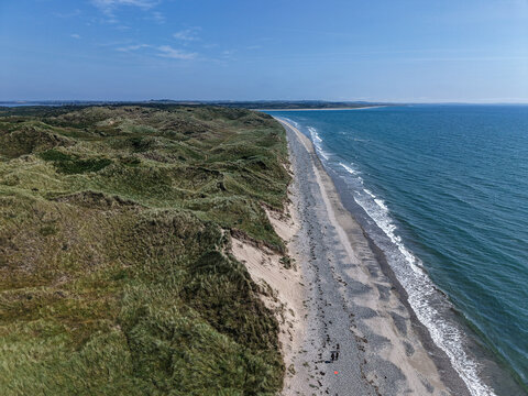 Aerial view of the coastline near Newcastle with rolling green sand dunes, a long pebble beach, and the blue sea under a clear sky in Newcastle, Northern Ireland, United Kingdom.