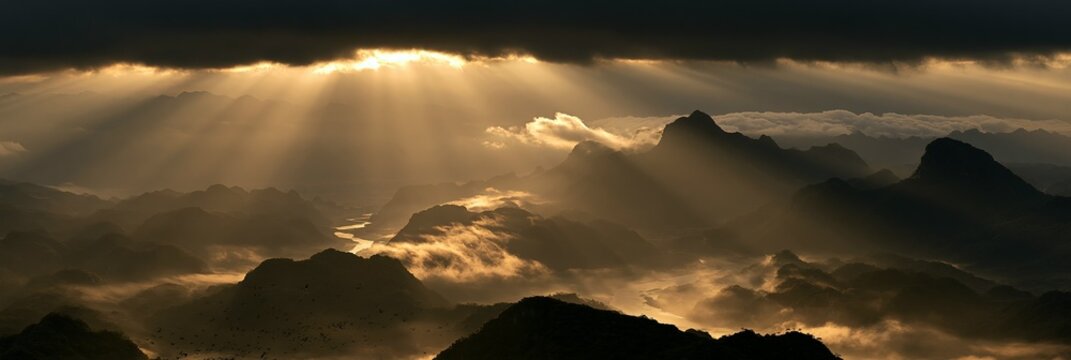 a breathtaking view of a mountainous range bathed in golden light. The suns rays pass through the clouds, creating a radiant glow that contrasts with the dark, stormy sky.