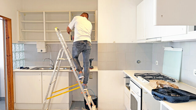 Professional handyman assembling hanging kitchen cabinets on stepladder during home renovation