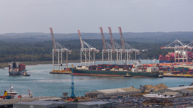 Aerial view of the busy Port of Southampton with large container ships, towering gantry cranes, and stacks of colorful cargo containers in Southampton, England, United Kingdom.