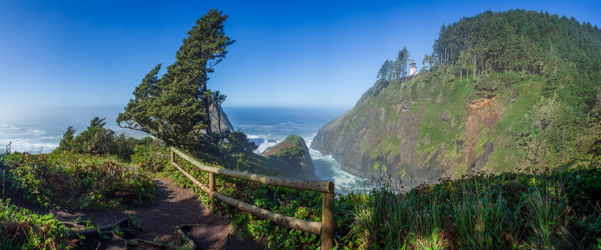 Beautiful wide panoramic view of a fenced hiking trail overlooking a historic lighthouse on a cliff over the ocean