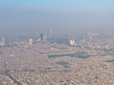 Aerial view of the sprawling cityscape with dense urban development, high-rise buildings, and hazy atmosphere in Surabaya, East Java, Indonesia.