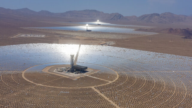 Aerial view of a large concentrated solar power plant with thousands of mirrors and central solar towers in a desert landscape, United States.