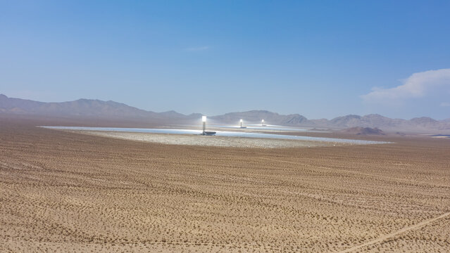 Aerial view of a large concentrated solar power plant with thousands of mirrors and central solar towers situated in a vast desert landscape in the United States.