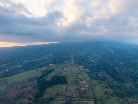 Aerial view of the rural landscape in Ngajum featuring agricultural fields and lush vegetation under a cloudy sky in Ngajum, East Java, Indonesia.