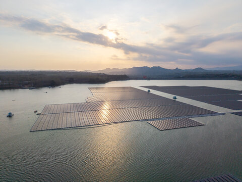 Aerial view of the floating solar farm on the Sutami Dam reservoir at sunset, with mountains in the background in Kecamatan Sumberpucung, Jawa Timur, Indonesia.