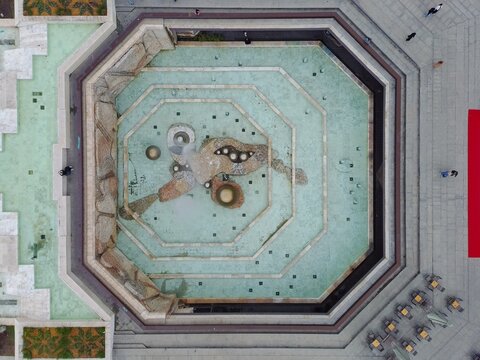 Aerial view of the NDK square fountain with its octagonal design and turquoise water surrounded by stone paving, cafe tables, and people walking in Sofia, Sofia City Province, Bulgaria.