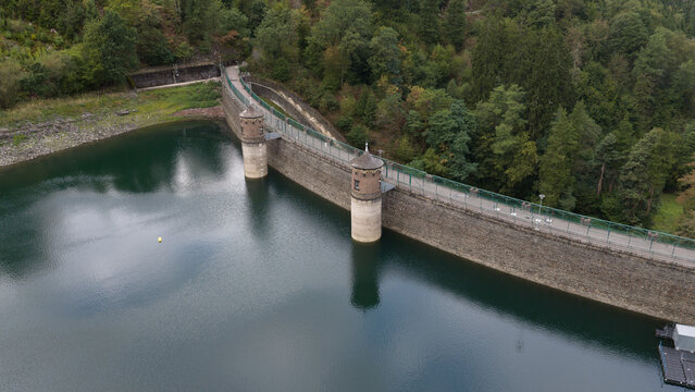 Aerial view of the historic stone dam wall of Sengbachtalsperre with its two towers and calm reservoir water surrounded by dense forest in Solingen, Nordrhein-Westfalen, Germany.