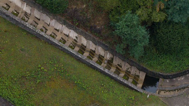 Aerial view of the concrete stepped spillway of the Sengbachtalsperre dam surrounded by lush green vegetation and stone walls in Solingen, Nordrhein-Westfalen, Germany.