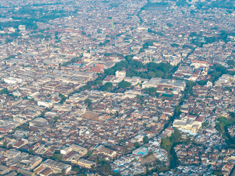Aerial view of the dense urban landscape of Malang featuring residential rooftops, lush green trees, and intricate street patterns in Malang, East Java, Indonesia.