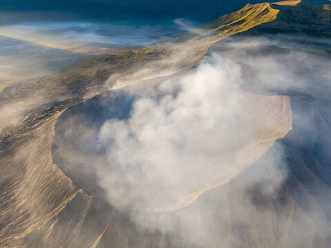 Aerial view of Mount Bromo crater emitting volcanic smoke with rugged slopes and morning light in Tosari, East Java, Indonesia.