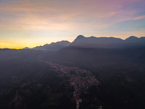 Aerial view of Wonotoro village nestled in the valley during sunset with surrounding mountains and soft golden light in Sukapura, East Java, Indonesia.
