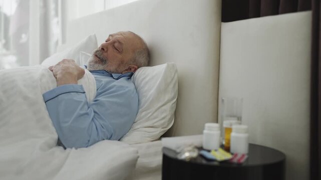 Elderly man sleeping in bed with medication on bedside table in care home