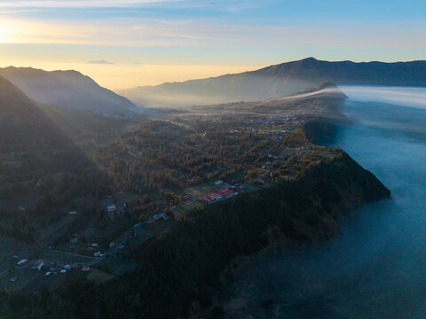 Aerial view of Cemorolawang village in the mountainous landscape of East Java, surrounded by morning mist and golden hour light, Kecamatan Sukapura, Jawa Timur, Indonesia.