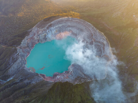 Aerial view of the turquoise acidic crater lake of Ijen volcano with sulfurous smoke rising from the rugged volcanic rim in Ijen, East Java, Indonesia.