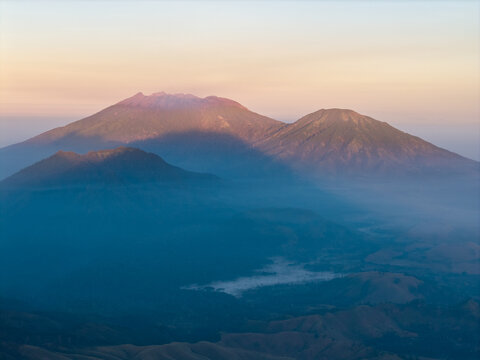 Aerial view of the Ijen volcano complex at sunrise with rugged mountain peaks, soft morning light, and mist settling in the valley below in Ijen, East Java, Indonesia.