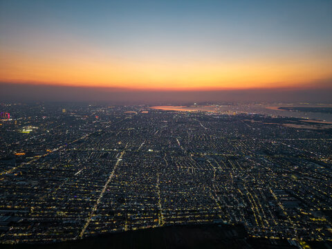 Aerial view of the sprawling cityscape of Surabaya at sunset, featuring dense urban rooftops, glowing street lights, and the distant coastline in Surabaya, East Java, Indonesia.