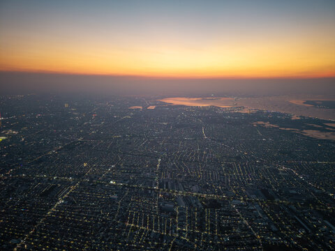 Aerial view of the sprawling city at sunset, with urban lights glowing across the dense residential grid and the coastline, Surabaya, East Java, Indonesia.