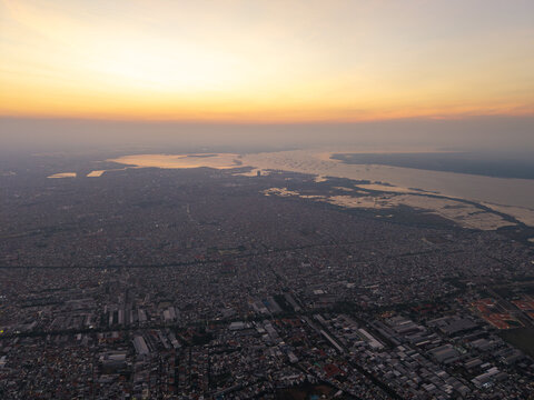 Aerial view of the historic Surabaya old town at sunset, featuring dense urban rooftops, industrial areas, and the coastline in Surabaya, East Java, Indonesia.