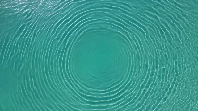 Gentle ripples emanating outward from a central point across the shimmering, turquoise surface of clear, pristine ocean water, creating mesmerizing circular patterns that suggest tranquility