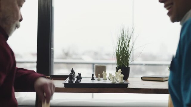 Young female nurse playing chess with aged man in nursing home, senior care