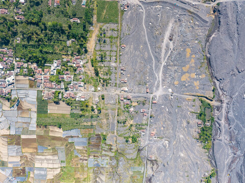 Aerial view of the aftermath of Mount Semeru's volcanic eruption, showing the contrast between Supiturang Village and the vast grey path of volcanic ash in Pronojiwo, East Java, Indonesia.