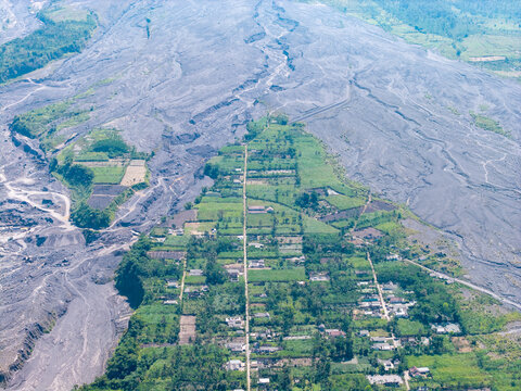 Aerial view of Supiturang Village showing the aftermath of the Mount Semeru eruption with volcanic ash deposits surrounding green fields and houses in Pronojiwo, East Java, Indonesia.