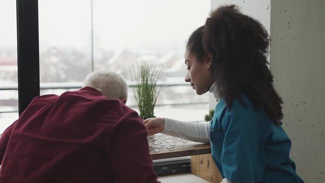 Female doctor and elderly male patient connect jigsaw pieces, improving memory