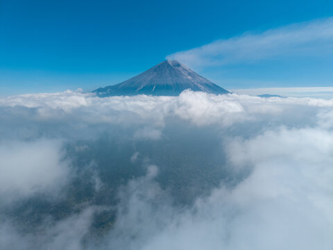 Aerial view of Semeru volcano rising above a thick layer of clouds with lush forest visible below in Pasrujambe, East Java, Indonesia.