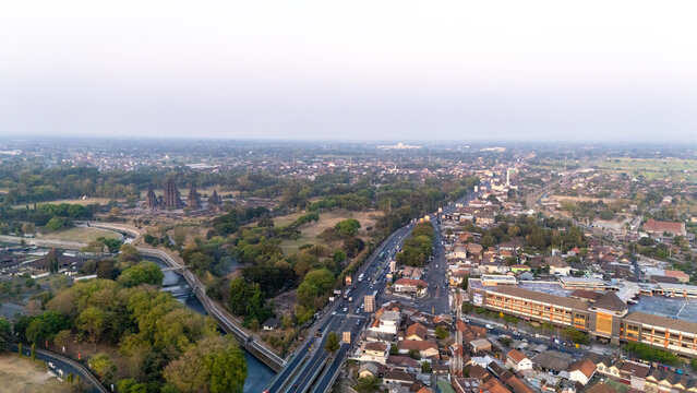 Aerial view of the ancient Prambanan Temple complex surrounded by lush greenery and urban development in Kecamatan Prambanan, Daerah Istimewa Yogya, Indonesia.