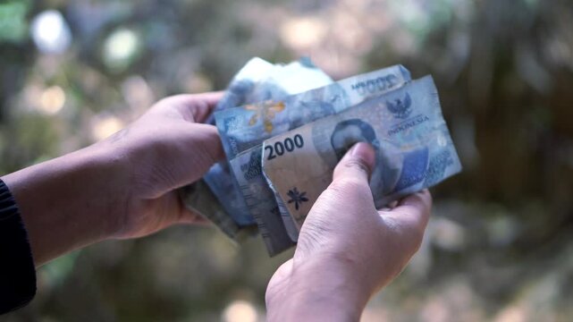 Close up view of hands holding a stack of two thousand Indonesian Rupiah banknotes.