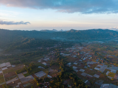Aerial view of Sumberurip village surrounded by terraced rice paddies and lush mountains under a soft morning sky in Pronojiwo, East Java, Indonesia.