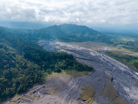 Aerial view of the lava path of Mount Semeru, featuring dark volcanic deposits cutting through lush green forests under a cloudy sky, Candipuro, East Java, Indonesia.