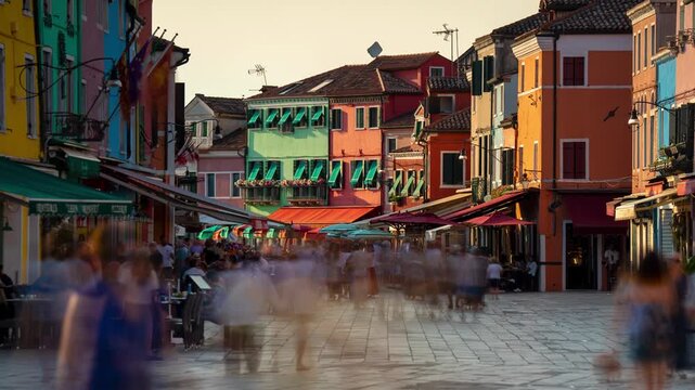 Burano island street timelapse with colorful houses, moving shadows, outdoor cafe dining, and blurred pedestrian crowd at sunset in Venice