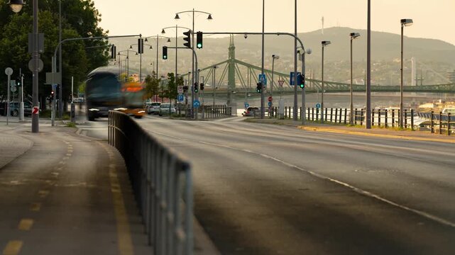 Golden hour time lapse of Budapest Danube embankment road with flowing traffic toward historic Liberty Bridge and Gellert Hill at sunset