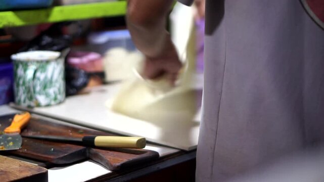 A vendor's hands stretching thin egg martabak dough on a prep table, showcasing the cooking skill of traditional Indonesian street food.
