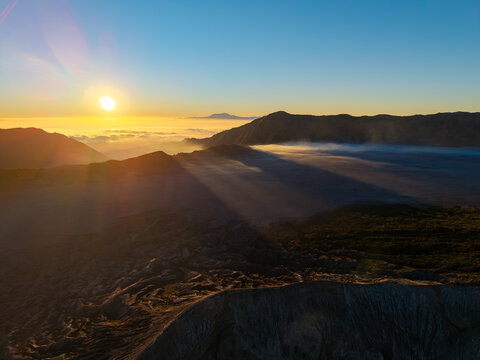 Aerial view of Mount Bromo at sunrise with golden light casting long shadows over the volcanic caldera and mist in Tosari, East Java, Indonesia.
