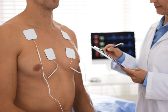 Doctor writing notes during patient's ECG test in clinic, closeup