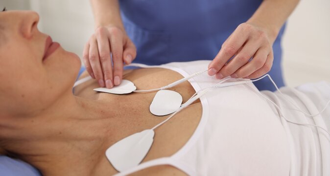 Doctor attaching ECG electrodes to patient's chest in clinic, closeup