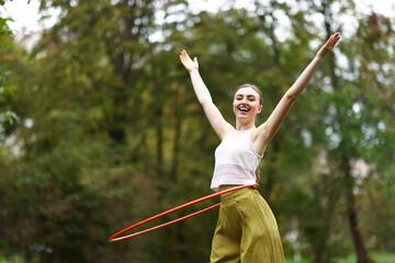 Athletic young woman exercising with hula hoop in park, space for text © New Africa