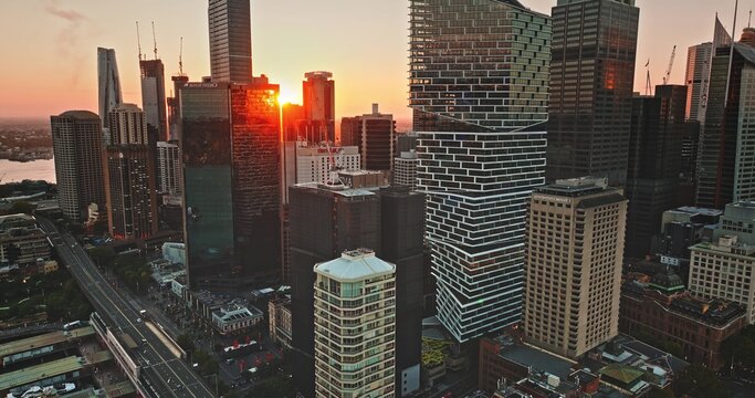 Sydney urban downtown business center area with modern architecture and towering skyscrapers buildings reflecting the warm orange glow of a beautiful sunset during evening. Aerial view drone flight