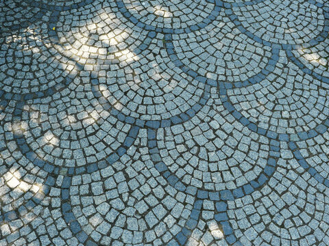 Natural stone paving with a repeating scallop pattern of interlocking arcs. Contrasting cobbles emphasize the geometry.